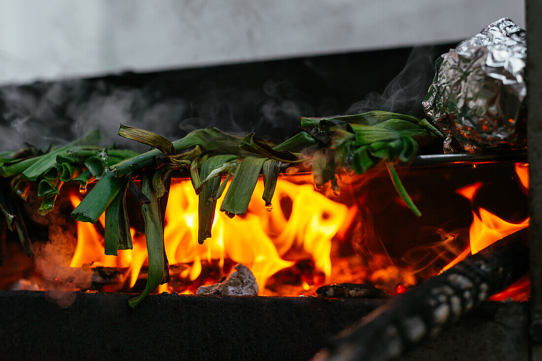 Heap of traditional Catalonian fresh green calcots on black metal hot grill with foil and burning charcoal placed on terrace