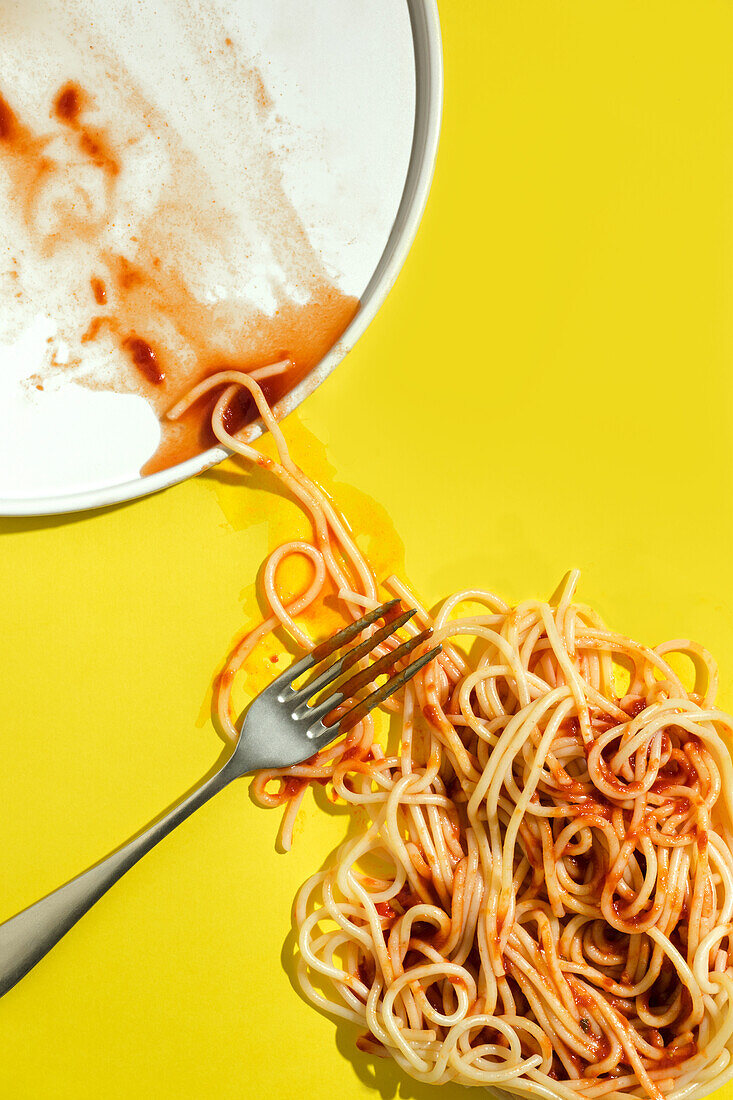 Von oben appetitliche gekochte Spaghetti mit roter Soße neben Teller und Gabel auf gelbem Hintergrund liegend