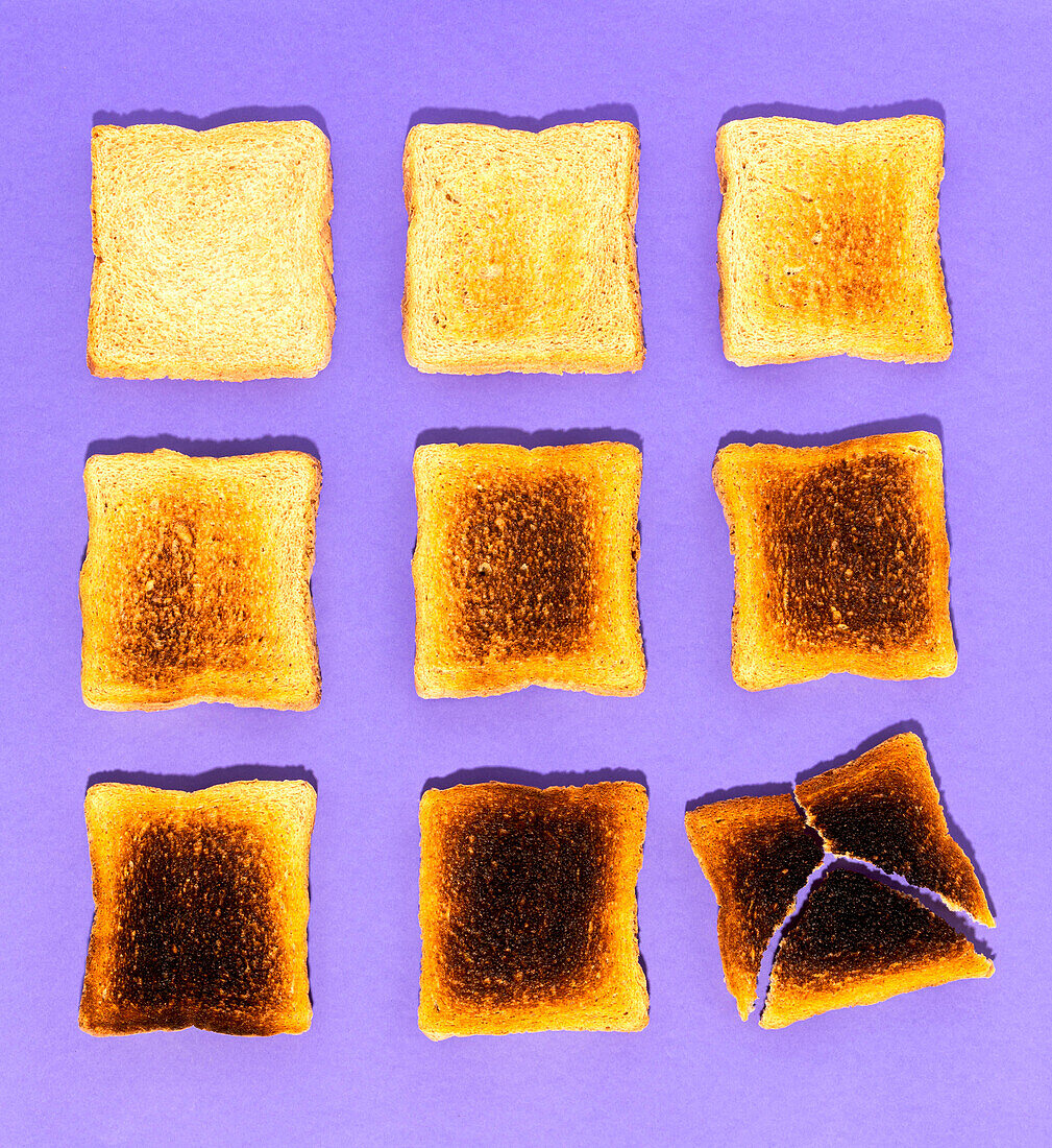 Top view of slices of bread ranging from fresh and soft to burnt and cracked against violet background