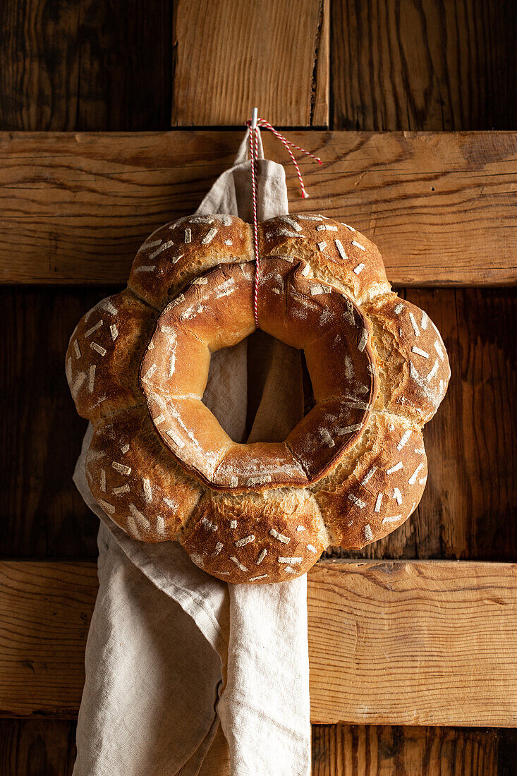 Decorative round baked loaf of bread with white patterns hanging on wooden wall with towel in light kitchen at home