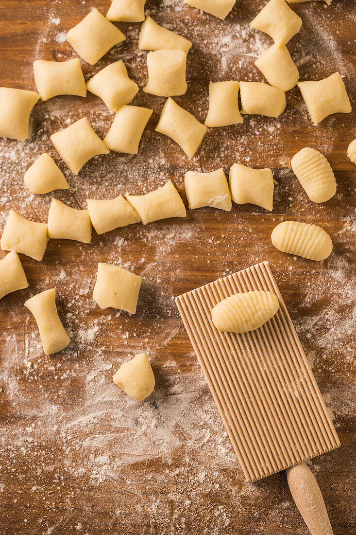 Top view of pieces of soft raw dough placed on wooden table covered with flour near ribber board during gnocchi preparation in the kitchen