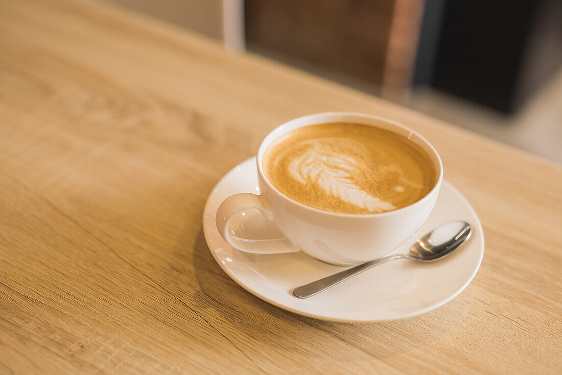 Blick von oben auf eine weiße Keramiktasse mit aromatischem, heißem Cappuccino, verziert mit Latte Art, auf einem Holztisch in einem Cafe