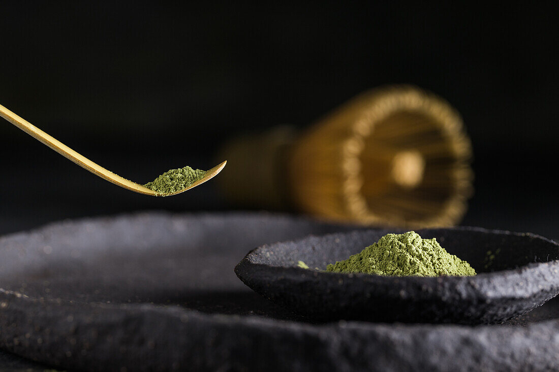 Spoon with dried matcha tea leaves on black tableware with chasen for traditional oriental ceremony