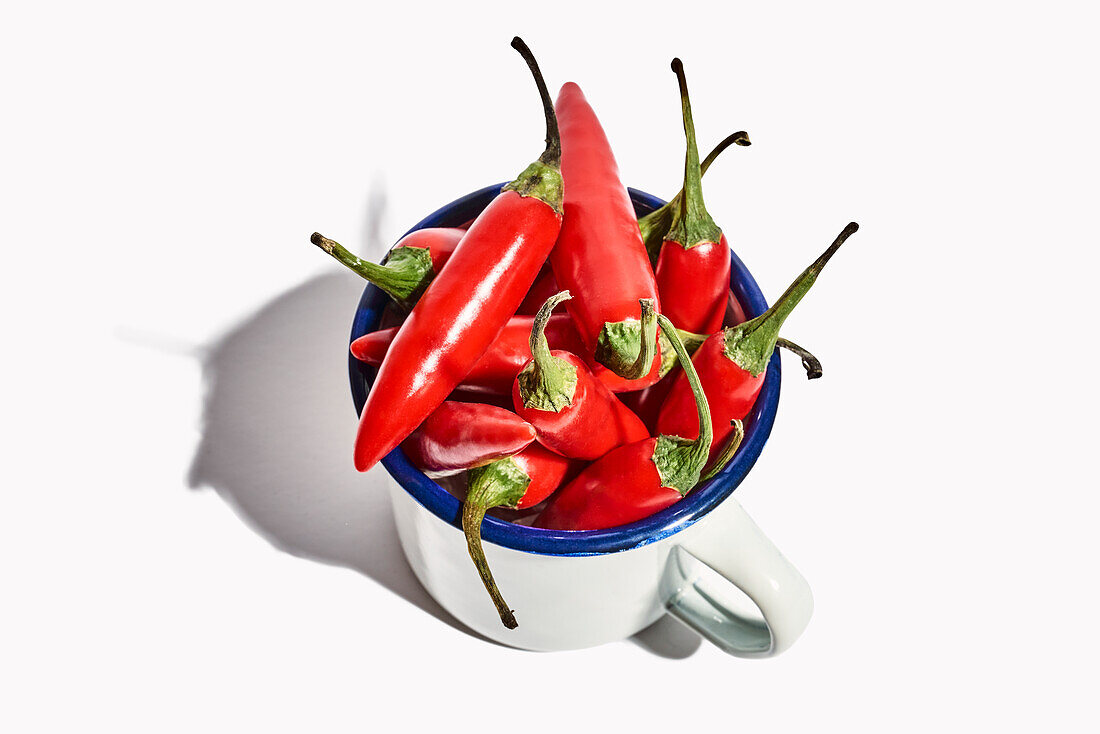 Top view of big ceramic mug full of ripe fresh exotic pepper placed on white background
