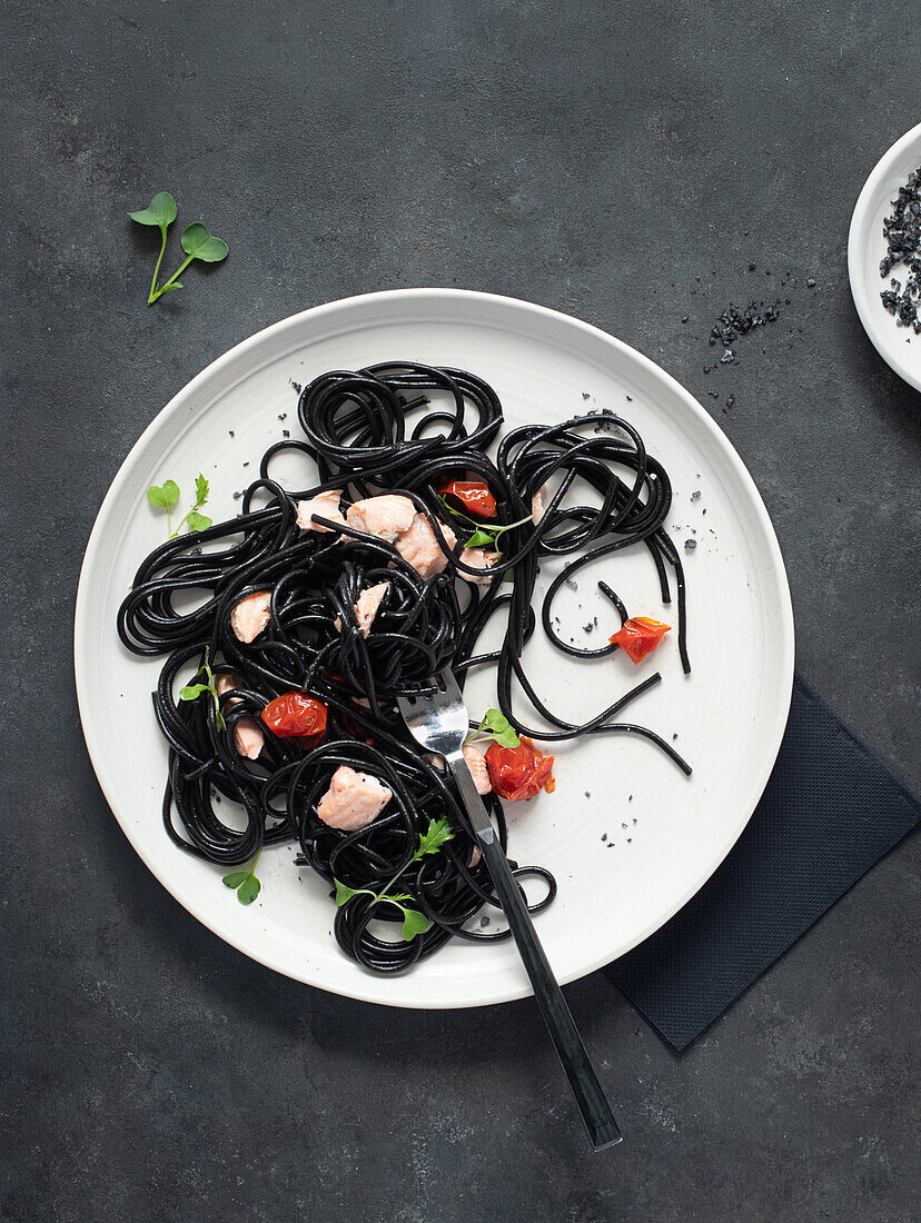 From above black ink spaghetti with salmon in ceramic plate on dark background