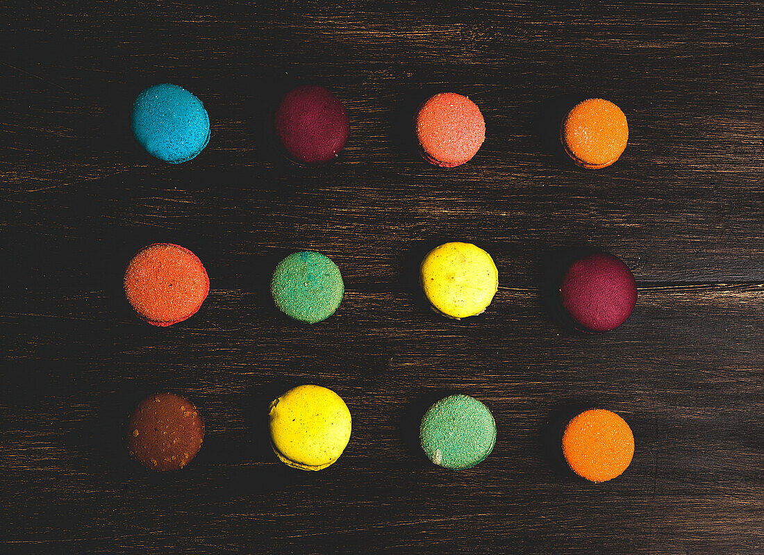 From above colorful French macaroons with various fillings placed on wooden table in dark background