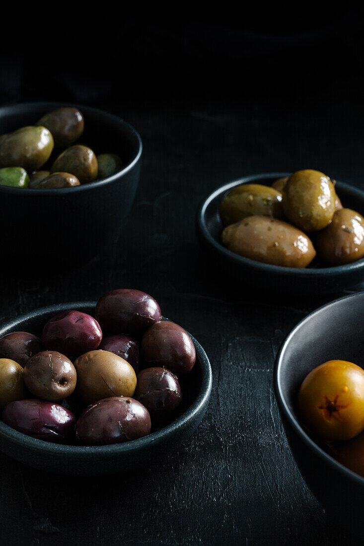 From above tasty juicy green brown yellow olives in black and white bowls on black table decorated with