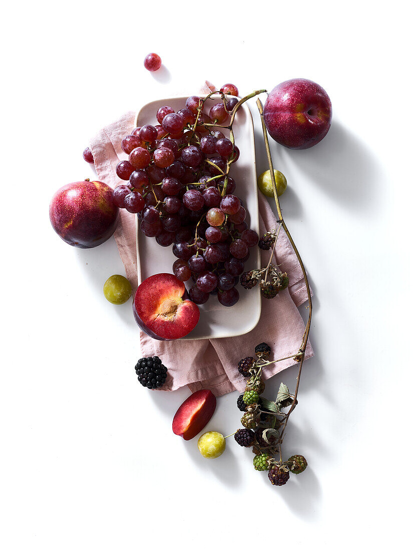 Composition with fresh summer fruits and berries on white background. Grapes, plums and apples in sunlight.