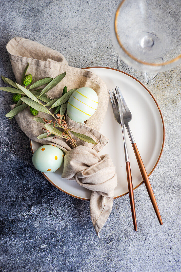 Von oben Besteck für ein Osteressen mit Olivenzweigen und Eiern auf einem Teller auf einem konkreten Hintergrund