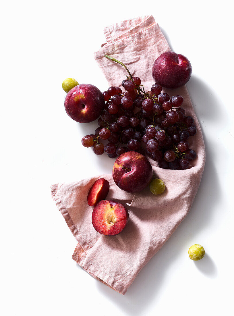 Frische Pflaumen und Weintrauben auf weißem Hintergrund. Lila Lebensmittel. Ernte-Konzept