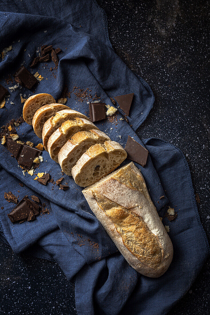 High angle of freshly baked cut bread loaf with chocolate bars placed on blue napkin on table in kitchen