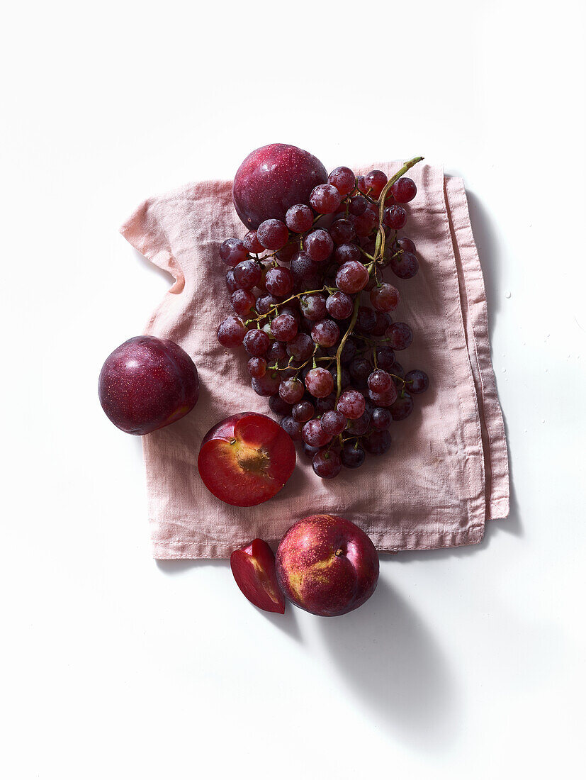Frische Pflaumen und Weintrauben auf weißem Hintergrund. Lila Lebensmittel. Ernte-Konzept