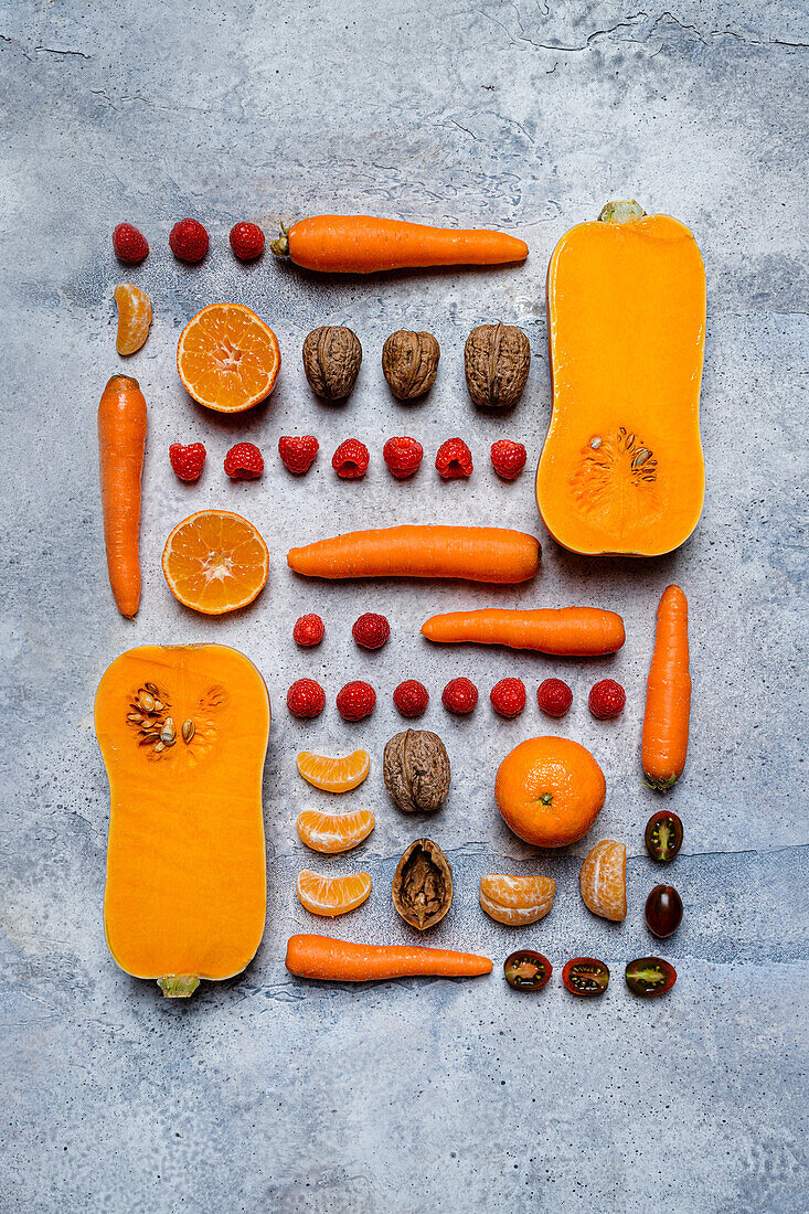 Still life of assorted aligned autumn veggies, sliced pumpkins, tomatoes, carrots, tangerines raspberries, and hazelnuts from above