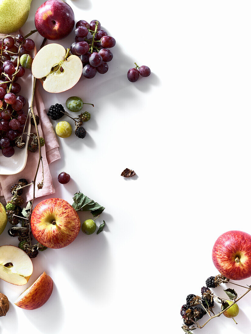 Composition with fresh summer fruits and berries on white background. Grapes, plums and apples in sunlight.