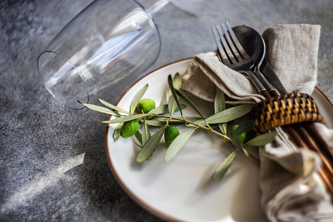 Rustikal gedeckter Sommertisch mit Tellern und Besteck, dekoriert mit Olivenzweigen