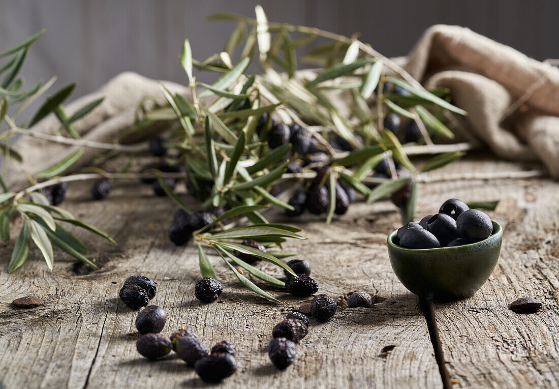 Small bowl of black pitted olives placed near green tree branches on shabby timber table in rustic kitchen