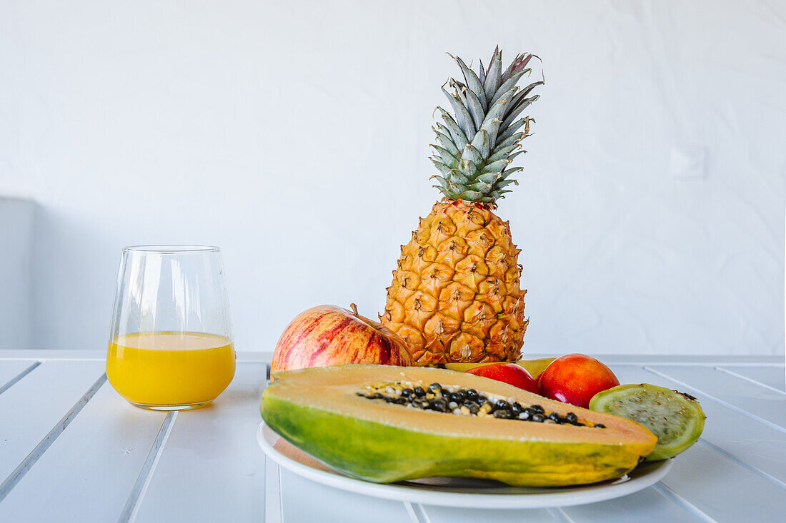 Delicious halved papaya served on plate near assorted colorful fruits and glass of fresh orange juice placed in white table