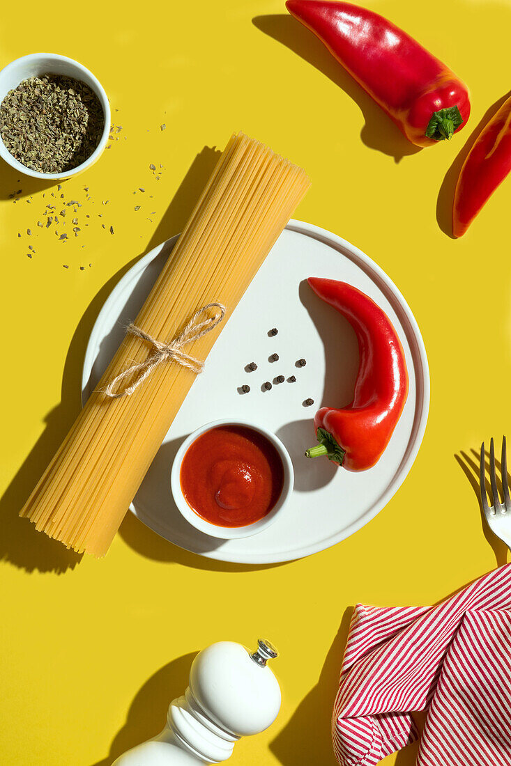 From above appetizing fresh dry spaghetti with red sauce and spice dip red peppers on yellow background