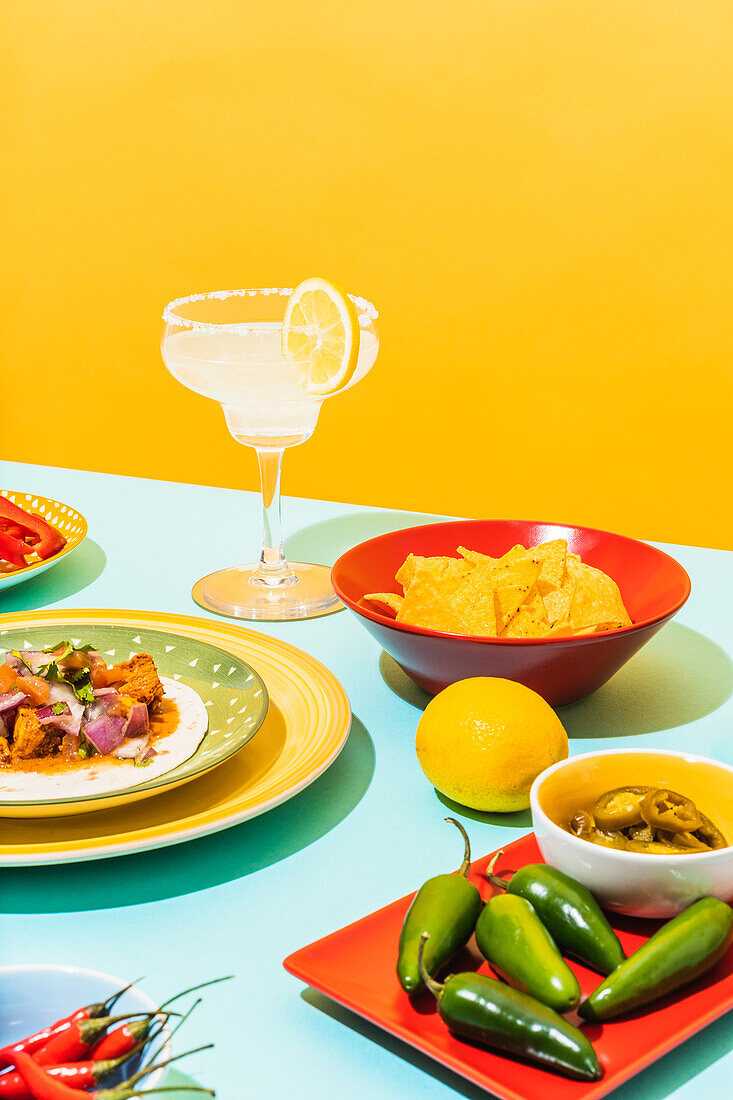 Fresh ingredients and traditional Mexican dishes placed near glass of cold lemonade on yellow background