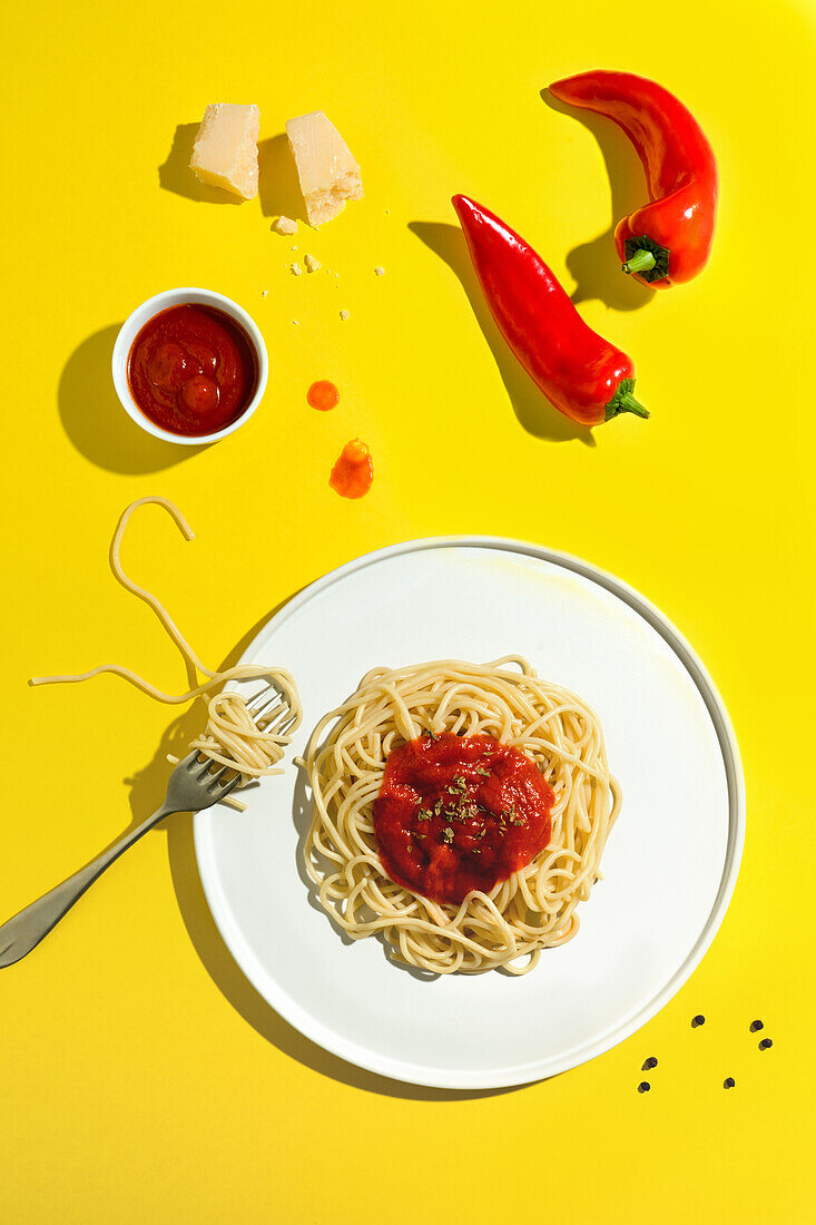Von oben appetitanregende frisch gekochte Spaghetti mit roter Soße und Gewürzdip, rote Paprika, Käse und Gabel auf gelbem Hintergrund