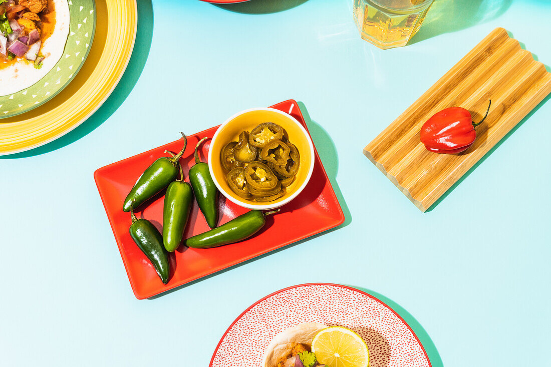 From above raw and marinated jalapenos placed on red plate on blue background