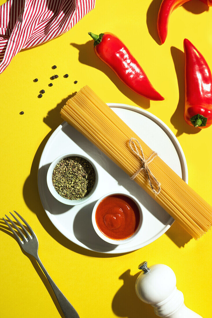 From above appetizing fresh dry spaghetti with red sauce and spice dip red peppers on yellow background