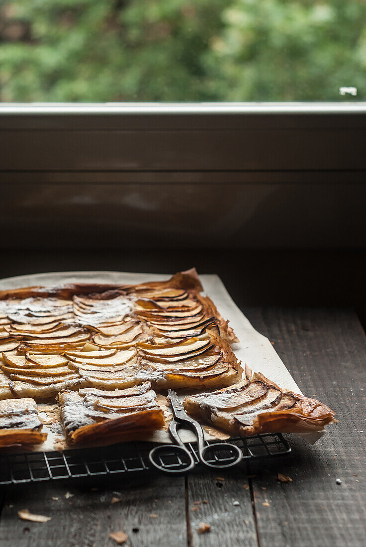 Delicious baked apple pie with frangipane cut into pieces and composed on cooling rack near window