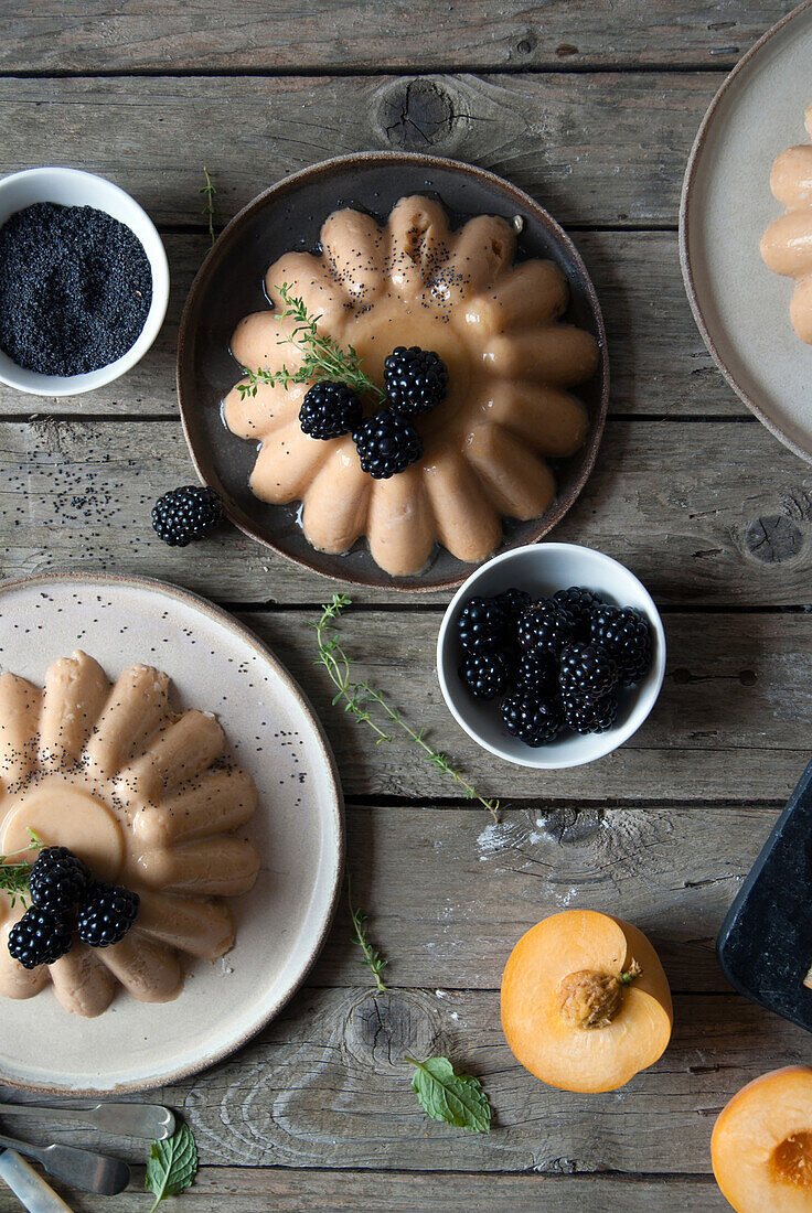 Flachaufnahme von angerichtetem Panna Cotta mit Pfirsich und Mohn auf Tisch mit Brombeeren