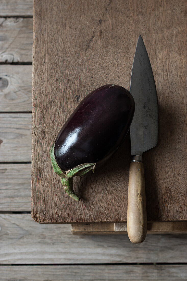 Fresh ripe eggplant with knife laid on wooden chopping board on box