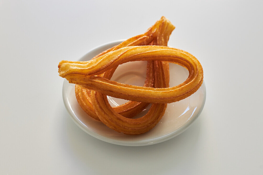 From above of crispy churros served on plate on white table in studio