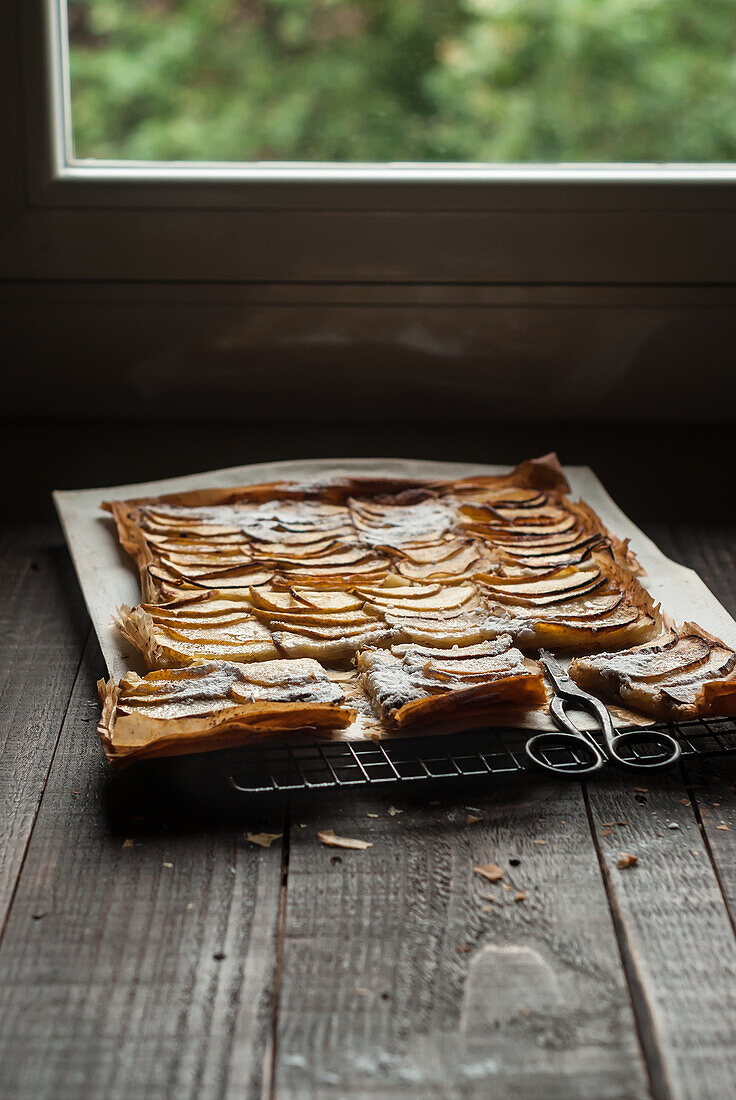 Köstlicher Bratapfelkuchen mit Frangipane, in Stücke geschnitten und auf einem Kühlregal am Fenster angerichtet