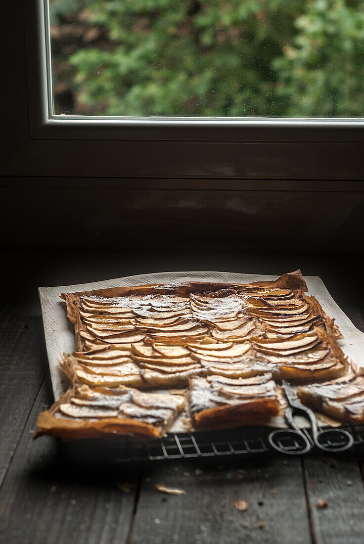 Delicious baked apple pie with frangipane cut into pieces and composed on cooling rack near window