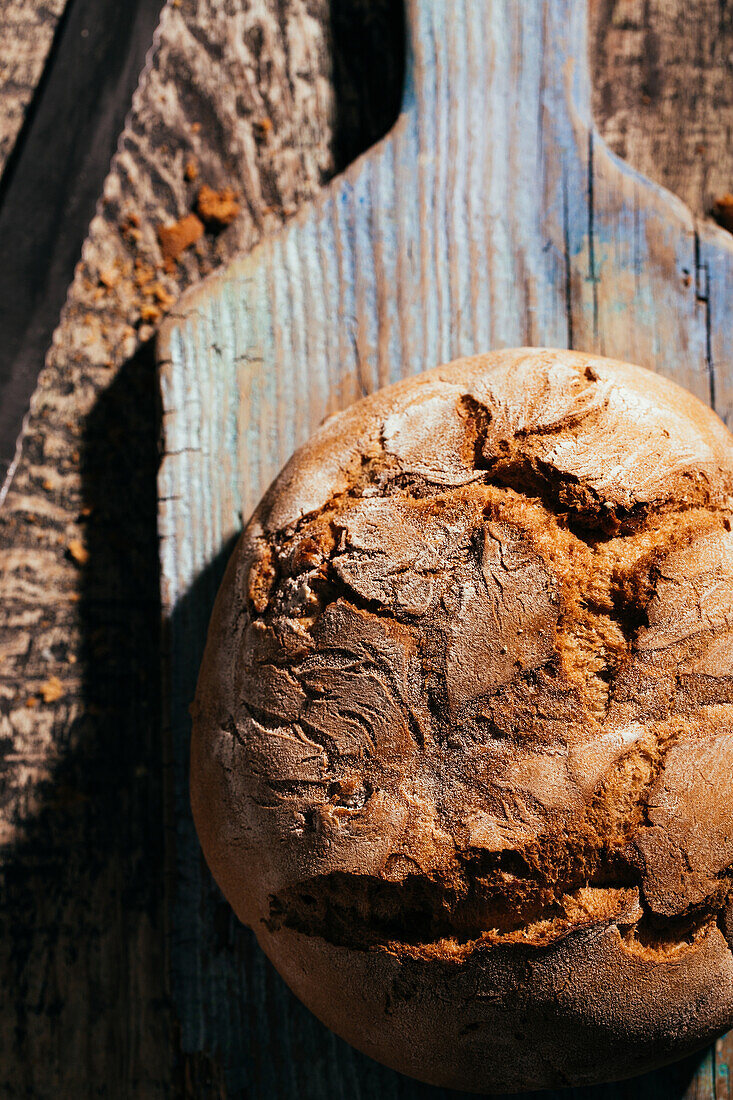 Draufsicht auf ein köstliches, frisch gebackenes Brot auf einem alten Schneidebrett auf einem Holztisch in der Küche