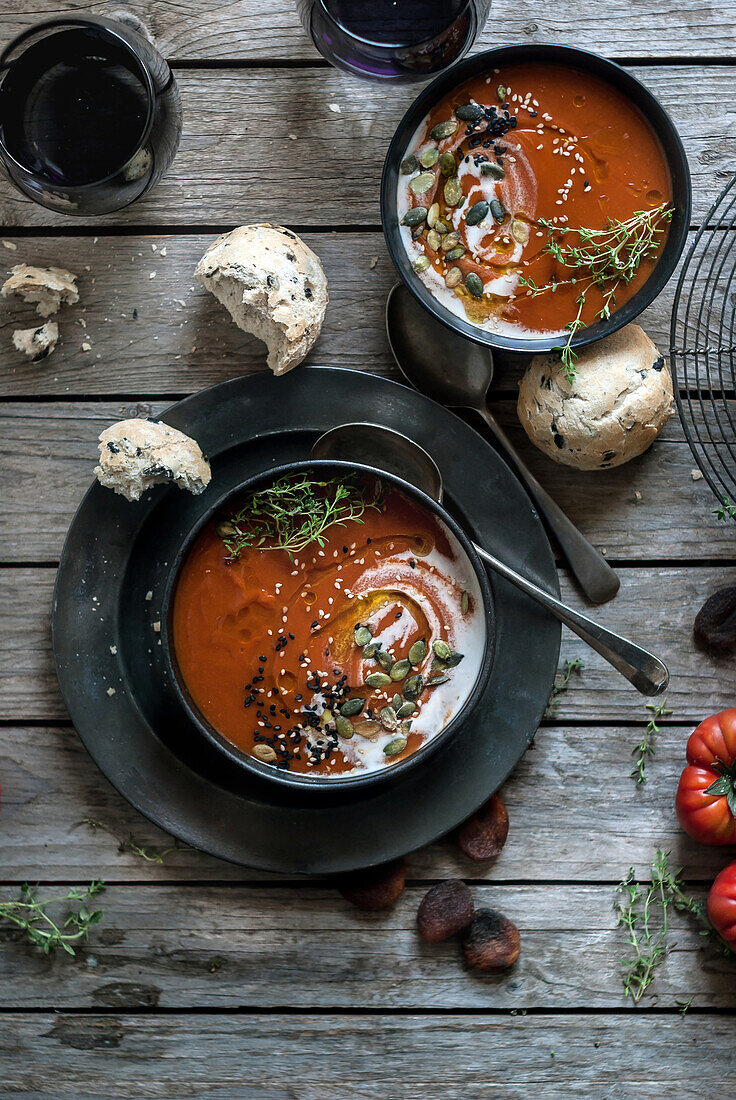 Flat lay of bowls with creamy tomato soup garnished with seeds and served on table with tomatoes and dried apricots