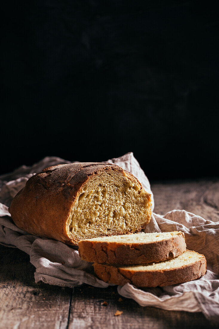 Freshly baked cut bread loaf placed on wooden table in kitchen on sunny day