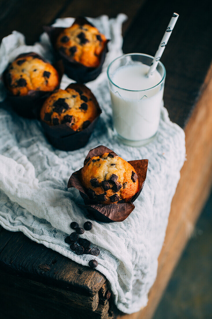 Leckere Muffins mit Schokoladenstückchen und ein Glas Milch auf dunklem Holzhintergrund