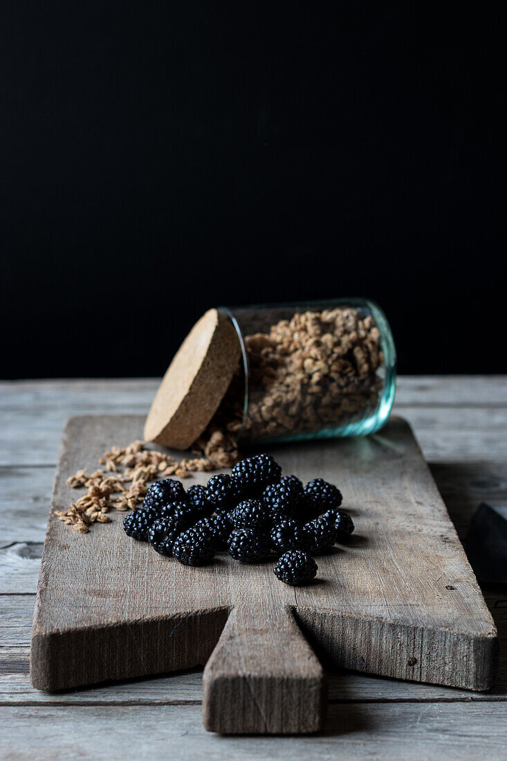 From above view of glass jar full of walnut granola and pile of blueberries placed on wooden cutting board on black background