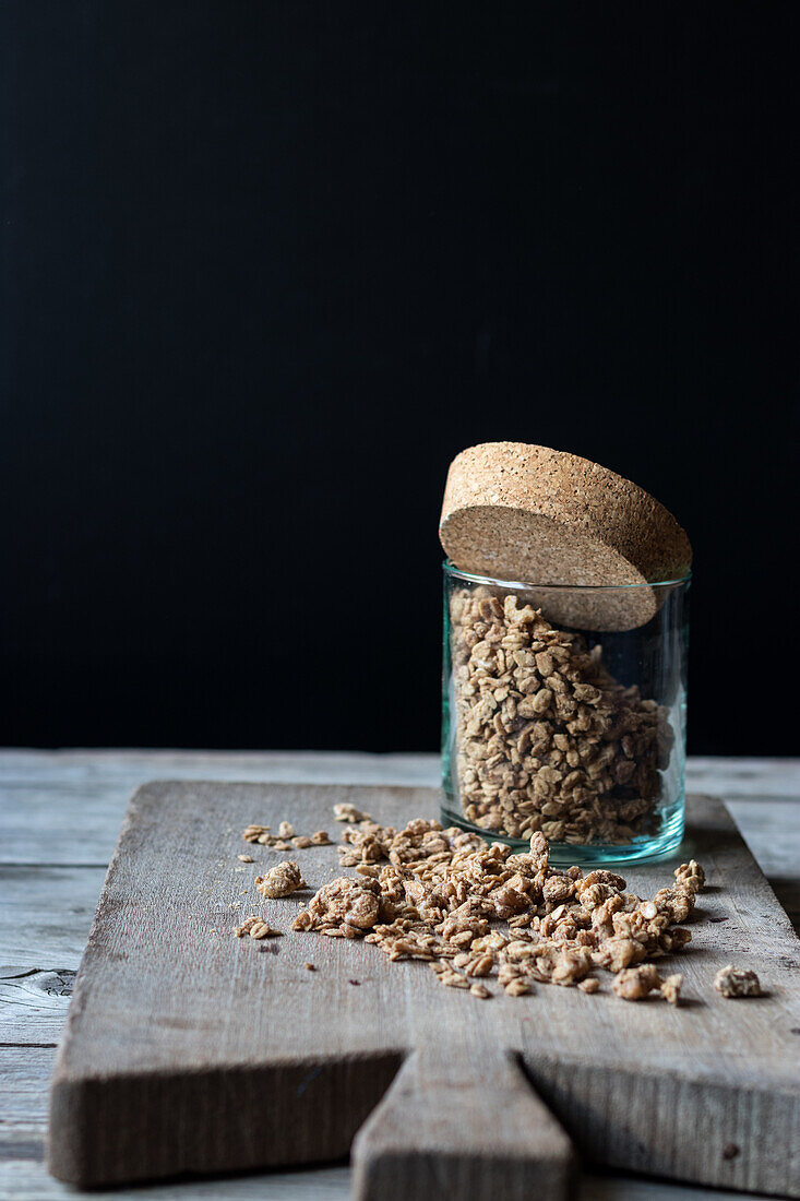 Glasgefäß mit Walnussmüsli auf einem Holzbrett vor schwarzem Hintergrund