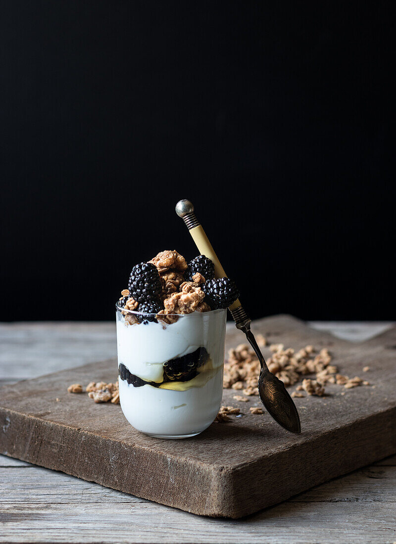 Closeup from above view of glass with walnut granola mixed with blueberries and yogurt placed on wooden chopping board near jar