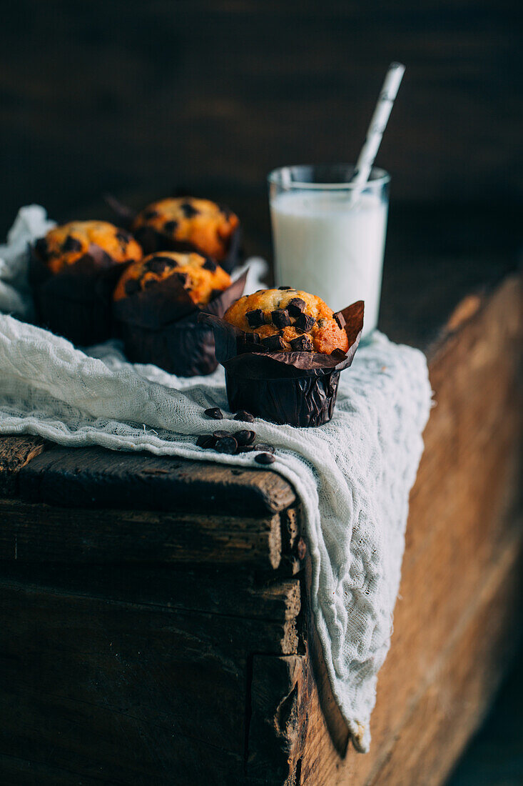 Leckere Muffins mit Schokoladenstückchen und ein Glas Milch auf dunklem Holzhintergrund