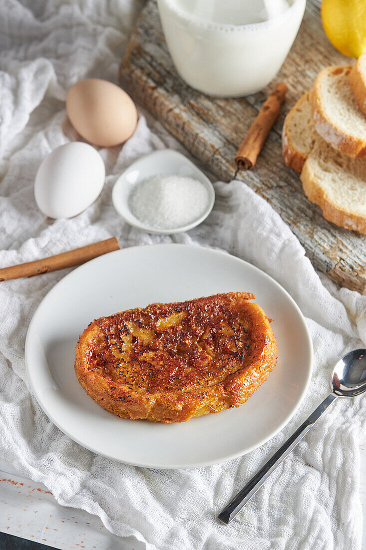 From above plate of appetizing Spanish torrija bread placed on table with raw eggs and sugar near wooden cutting board with jug of fresh milk and bread slices