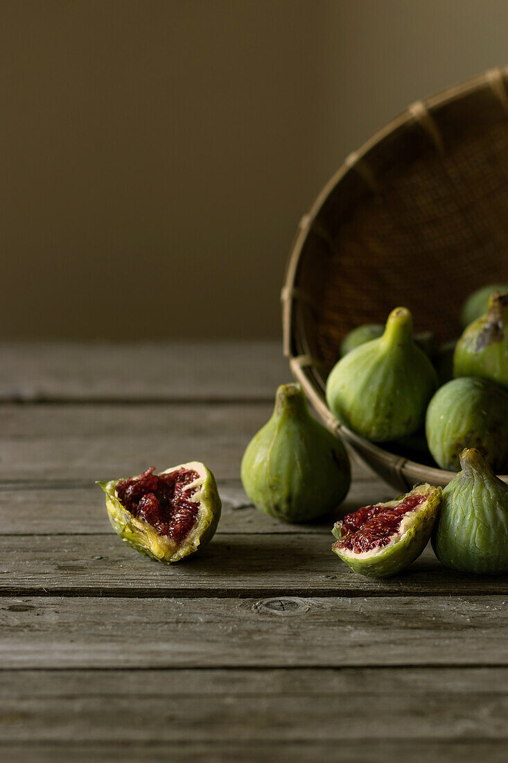 Closeup shot of basket with green figs and split fruit with red flesh on table