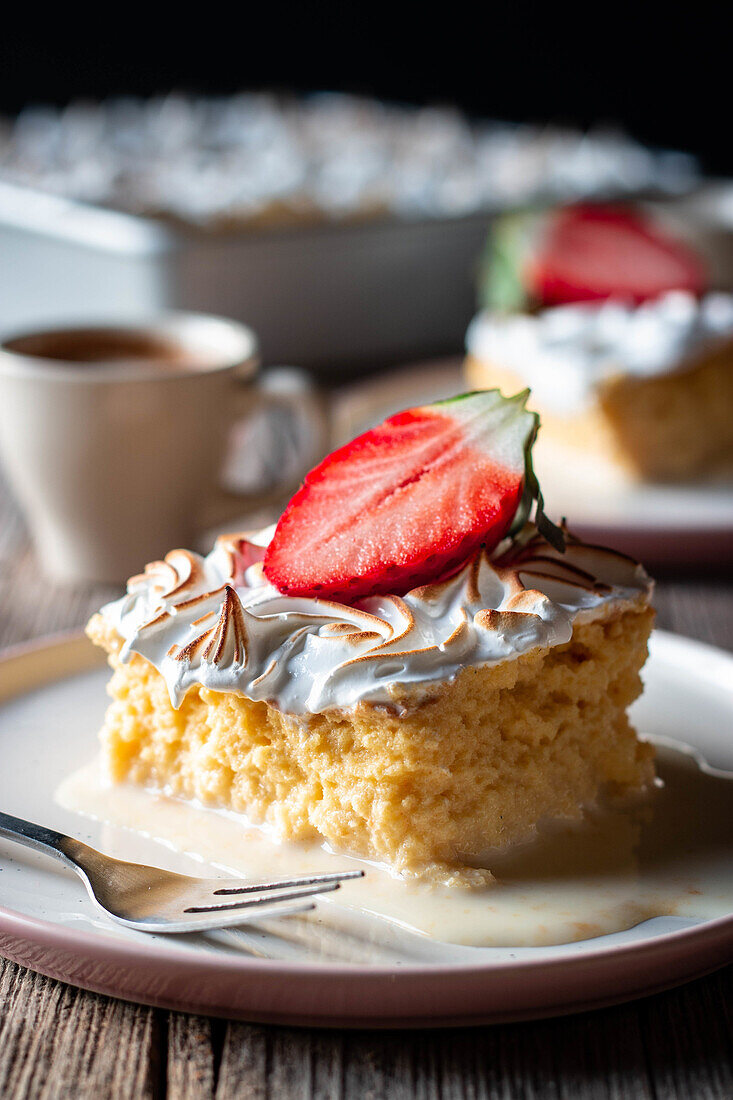 Sweet delicious piece of three milks cake with half fresh strawberry on white plate on wooden table