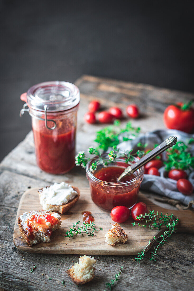 Small glass jar with fresh tomato jam placed near checkered napkin and green herbs on wooden table