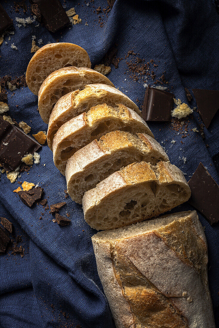 High angle of freshly baked cut bread loaf with chocolate bars placed on blue napkin on table in kitchen