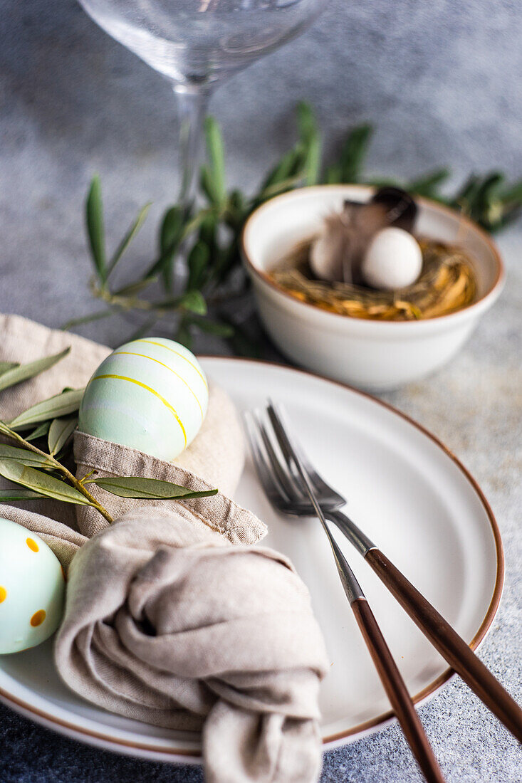 Cutlery set for Easter dinner with olive tree branches and eggs on a bird nest on a concrete background