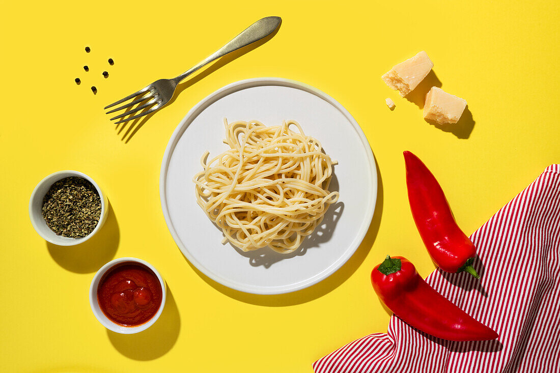 Von oben appetitanregende frisch gekochte Spaghetti mit roter Soße und Gewürzdip, rote Paprika, Käse und Gabel auf gelbem Hintergrund