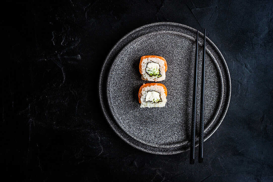 From above black stone plate with asian rolls and chopsticks