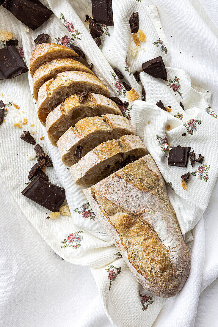 High angle of freshly baked cut bread loaf with chocolate bars placed on white napkin on table in kitchen