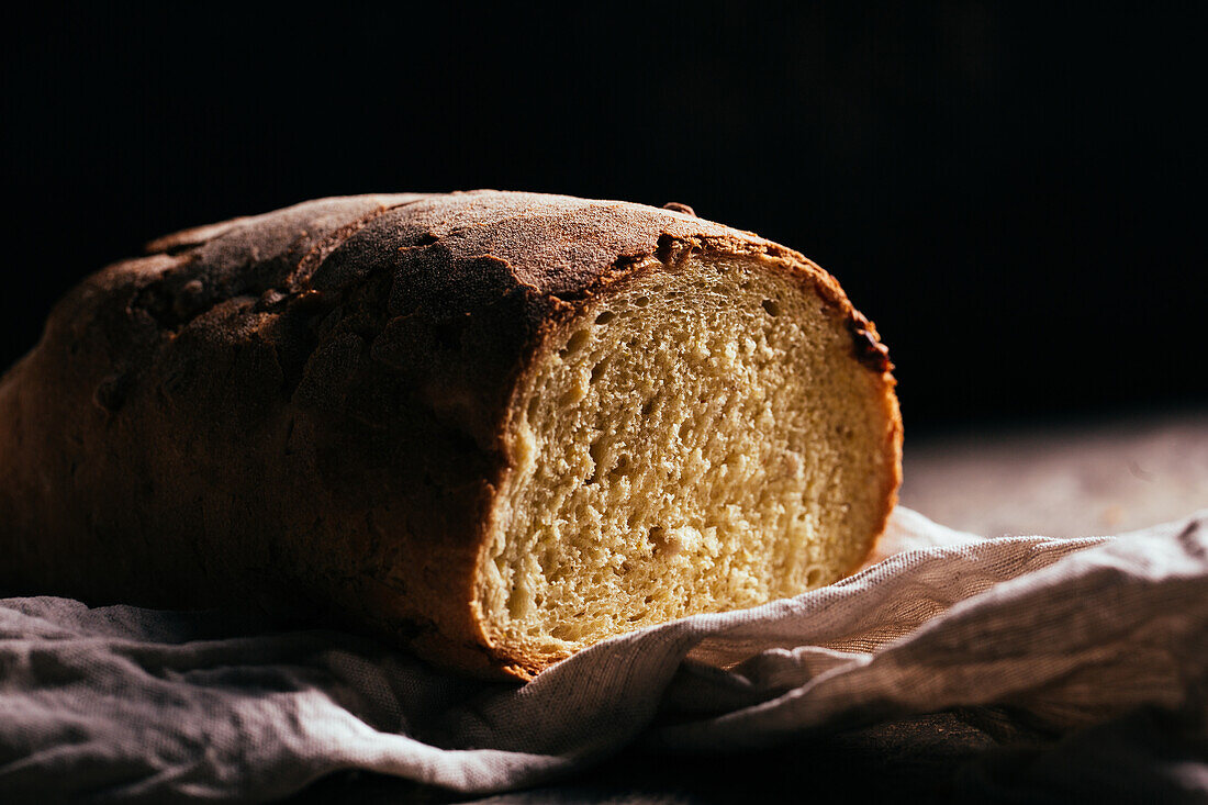 Freshly baked cut bread loaf placed on wooden table in kitchen on sunny day